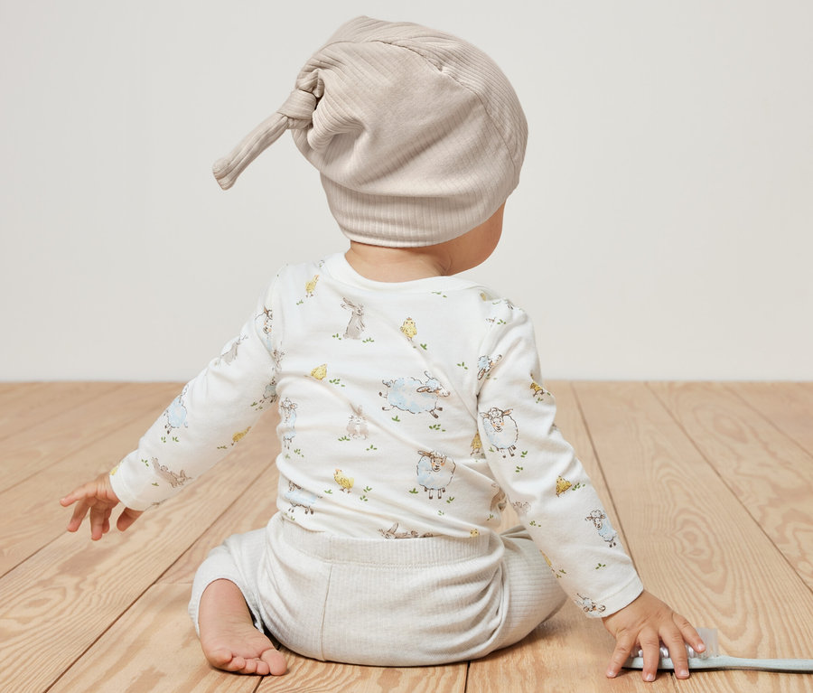 Bébé est assis dos à la caméra et porte 2 bonnets en jersey pour bébé.