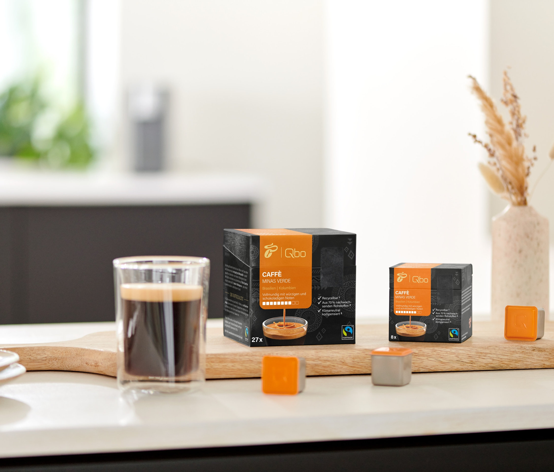 Sur une planche en bois, un verre de café à côté d'un paquet de Qbo Caffè MINAS VERDE et quelques capsules.