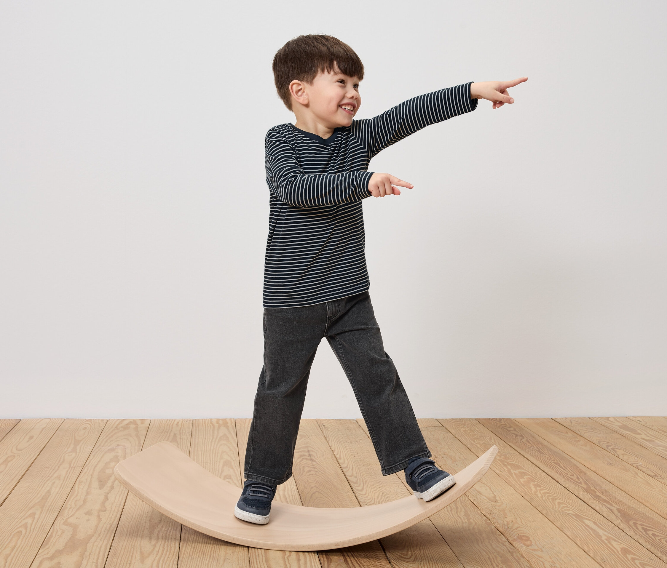 Un garçon se tient sur une planche d'équilibre en bois, rit et pointe du doigt.