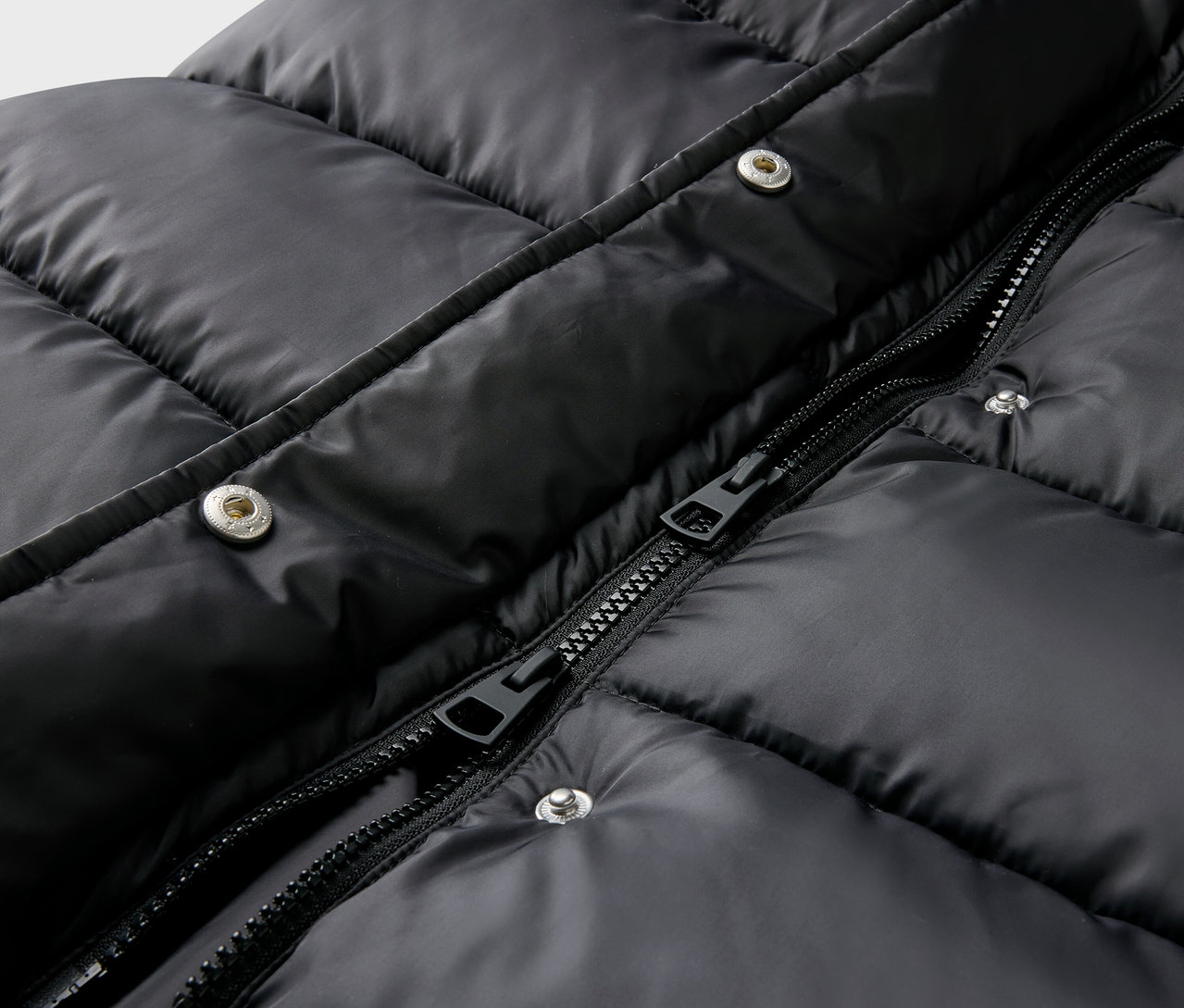 Gros plan sur une veste matelassée noire avec fermeture éclair et boutons-pression.
