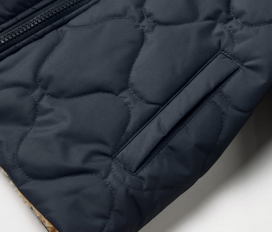 Détail d'une veste réversible matelassée pour enfant avec poche et fermeture éclair.