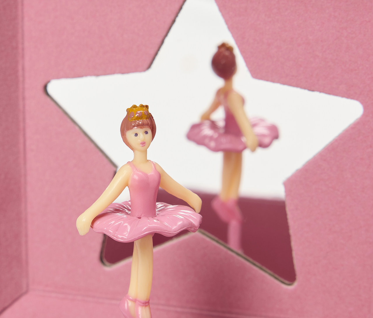 Une figurine de ballerine rose avec une couronne se tient devant un miroir en forme d'étoile.