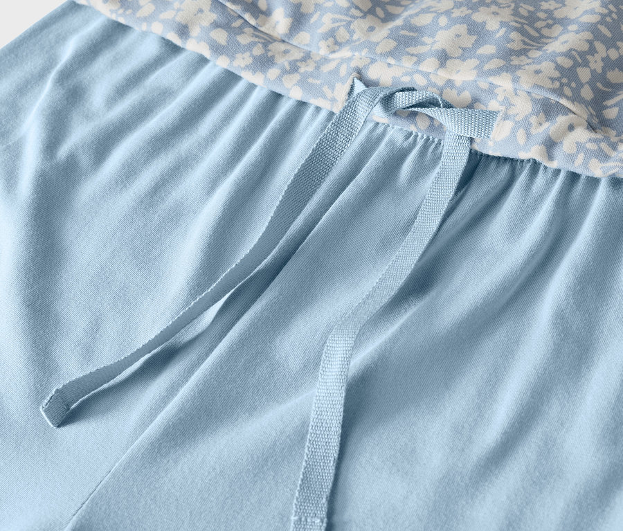 Détail d'un pantalon de pyjama bleu clair avec un haut à fleurs et un cordon de serrage.