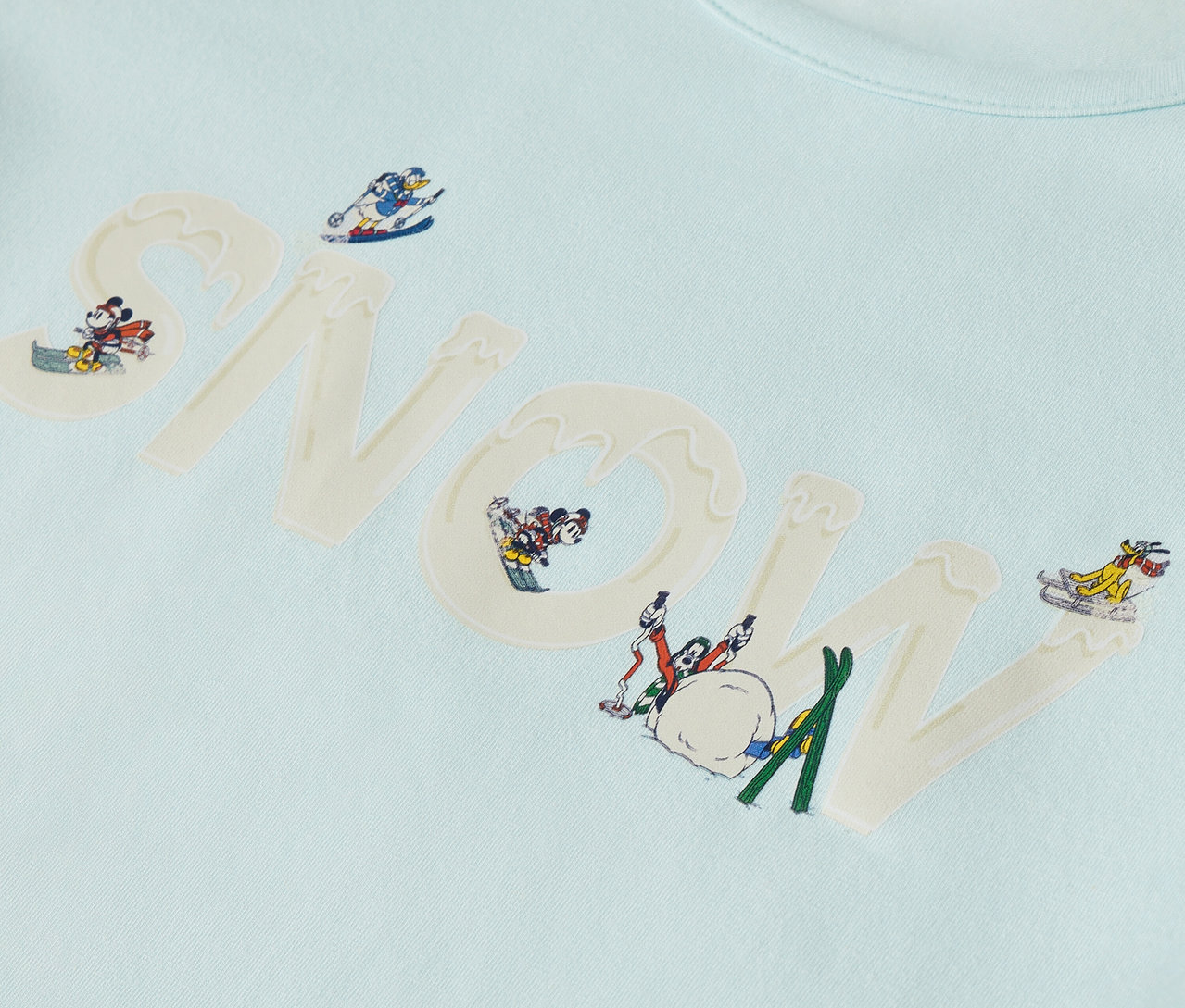 T-shirt bleu clair avec le mot « SNOW » et des personnages de dessins animés dans des scènes d'hiver.