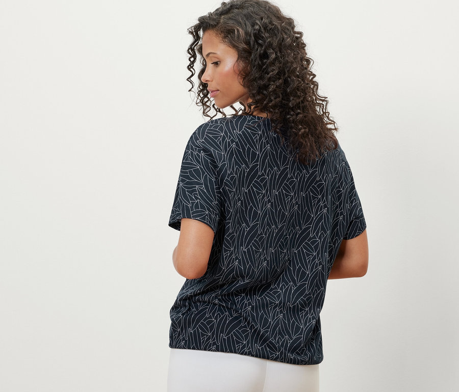 Vue arrière d'une femme aux cheveux bouclés portant un chemisier à encolure dégagée bleu foncé et un pantalon blanc.