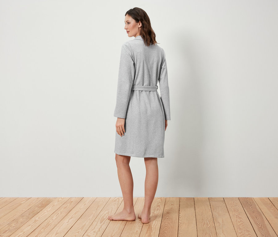 Une femme, vue de dos, porte un peignoir gris.