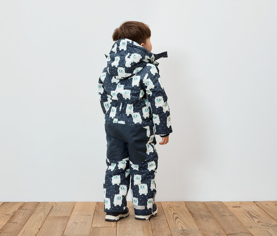 Un garçon, vu de dos, porte une combinaison bleu et blanche à capuche avec des motifs de bonhommes de neige.