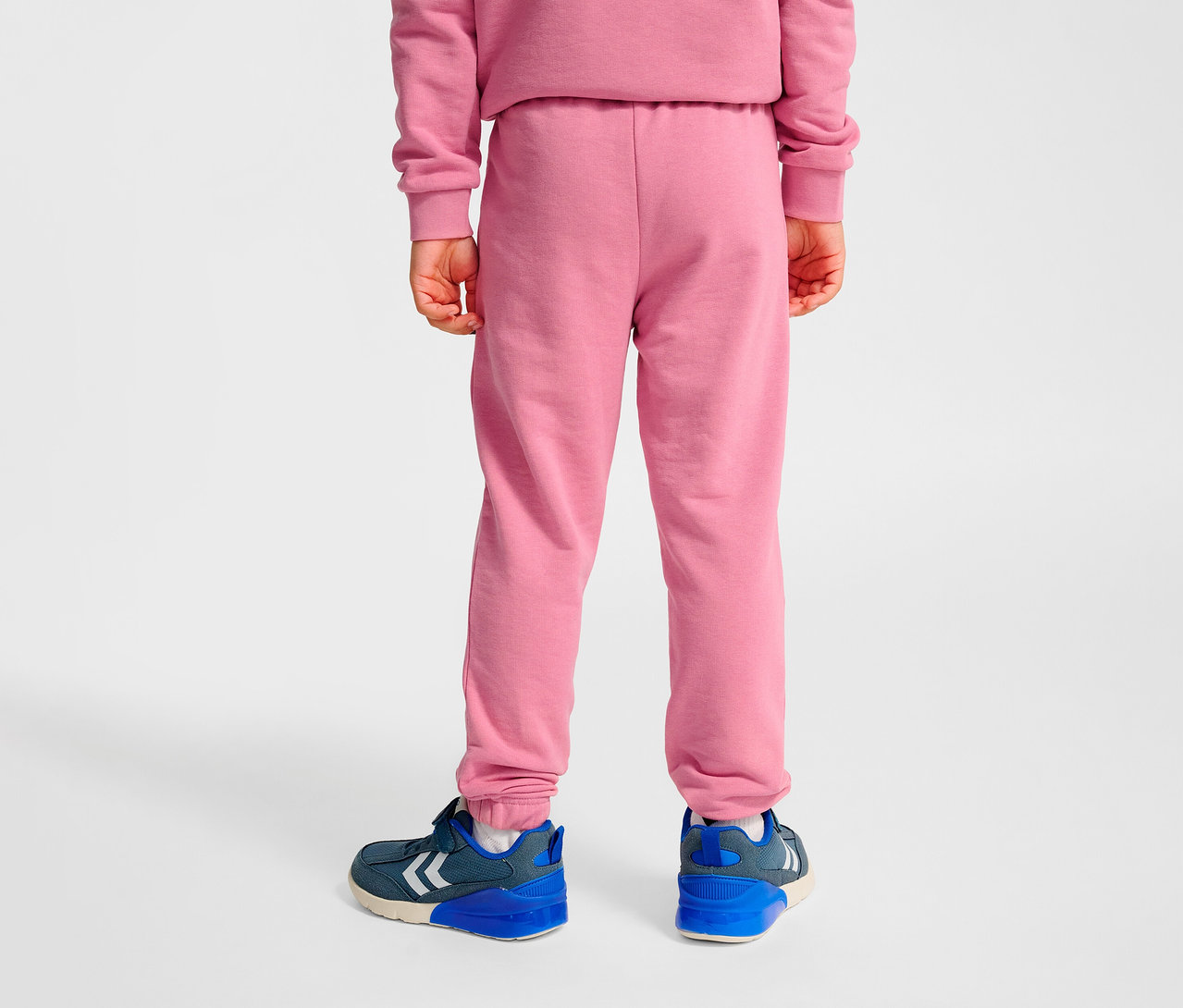 Vue arrière d'un enfant portant un pantalon régulier HUMMEL HMLJR Base rose et des chaussures bleues.