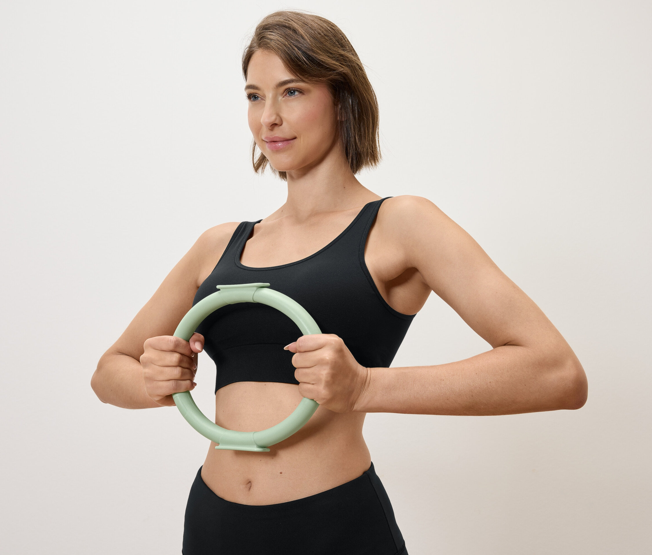 Femme tenant un cercle d'exercice vert clair devant elle, portant un haut de sport et un legging noirs.