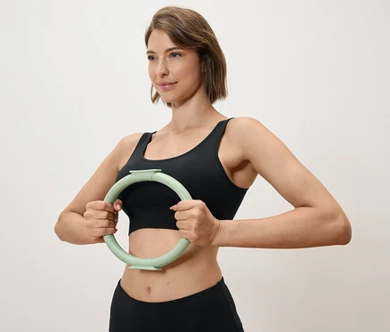 Femme tenant un cercle d'exercice vert clair devant elle, portant un haut de sport et un legging noirs.