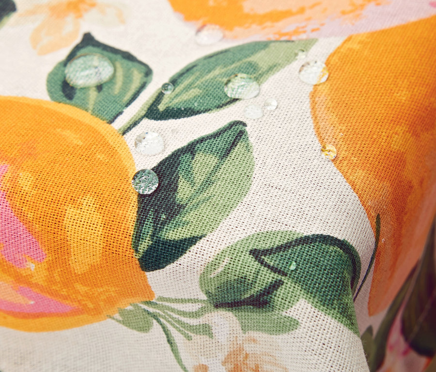 Détail d'une nappe lavable avec un motif d'oranges et de fleurs, sur laquelle reposent des gouttes d'eau.