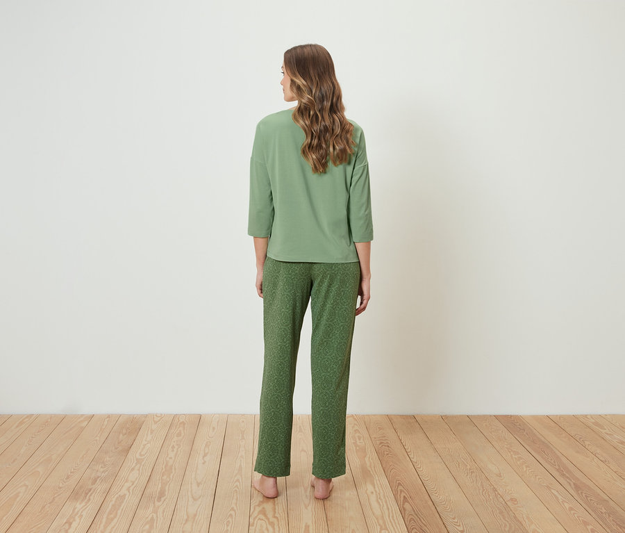 Une femme se tient dos à l'appareil photo et porte un pyjama vert.