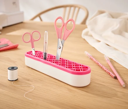 Des ciseaux et un crayon sont placés dans un organiseur polyvalent sur une table en bois.
