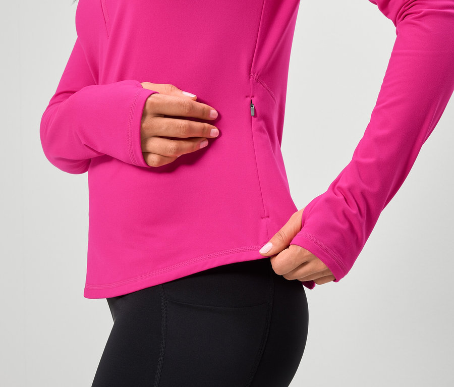 Une femme porte un haut rose à manches longues et un legging noir.