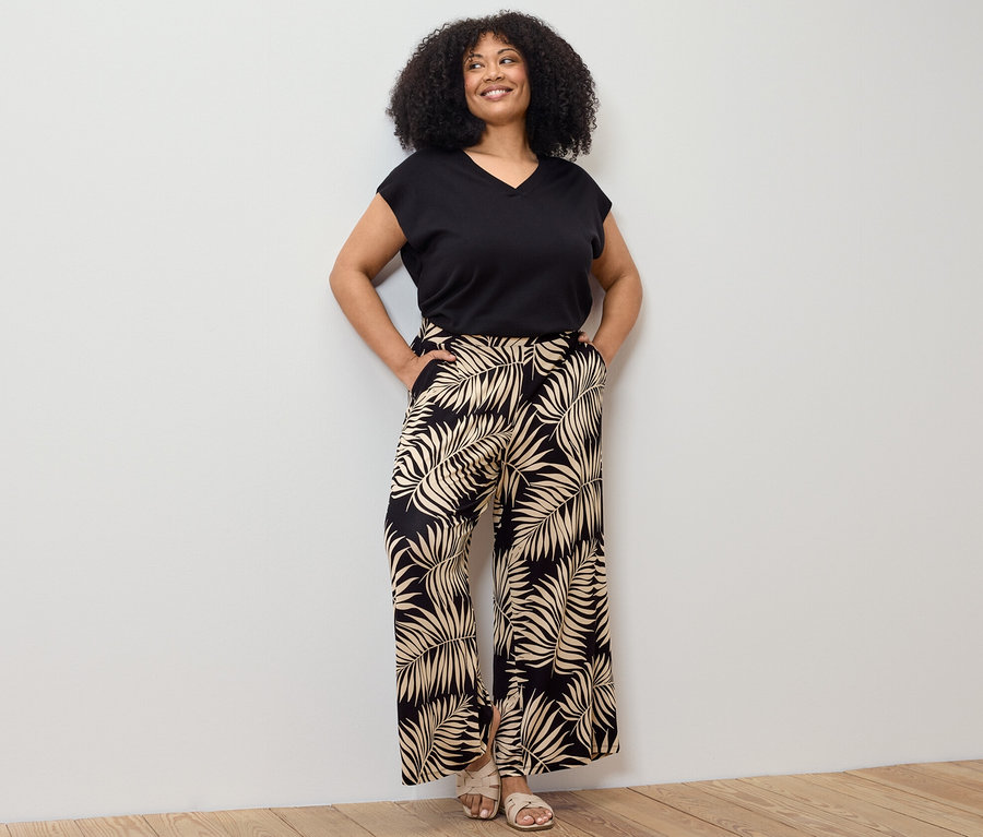 Femme posant dans un pull-over en maille fine à manches courtes noir et un pantalon palazzo imprimé.