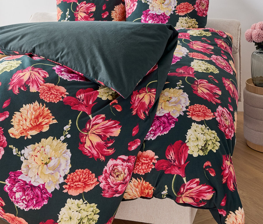 Linge de lit à fleurs sur un lit avec une couverture vert foncé.