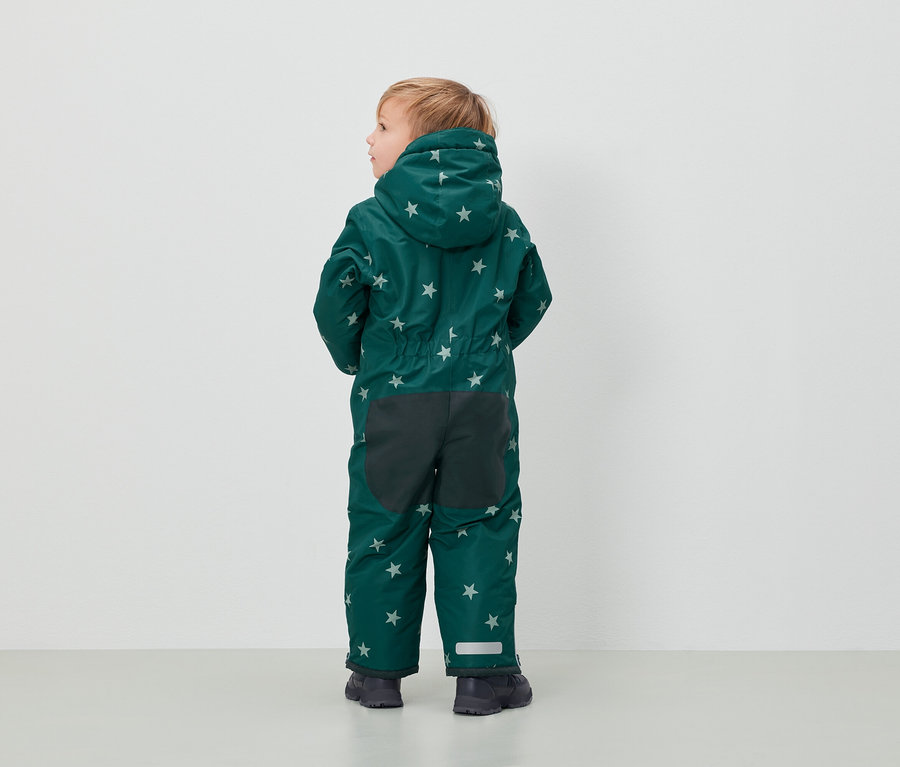 Un garçon en combinaison verte à motifs d'étoiles se tient dos à l'appareil photo.