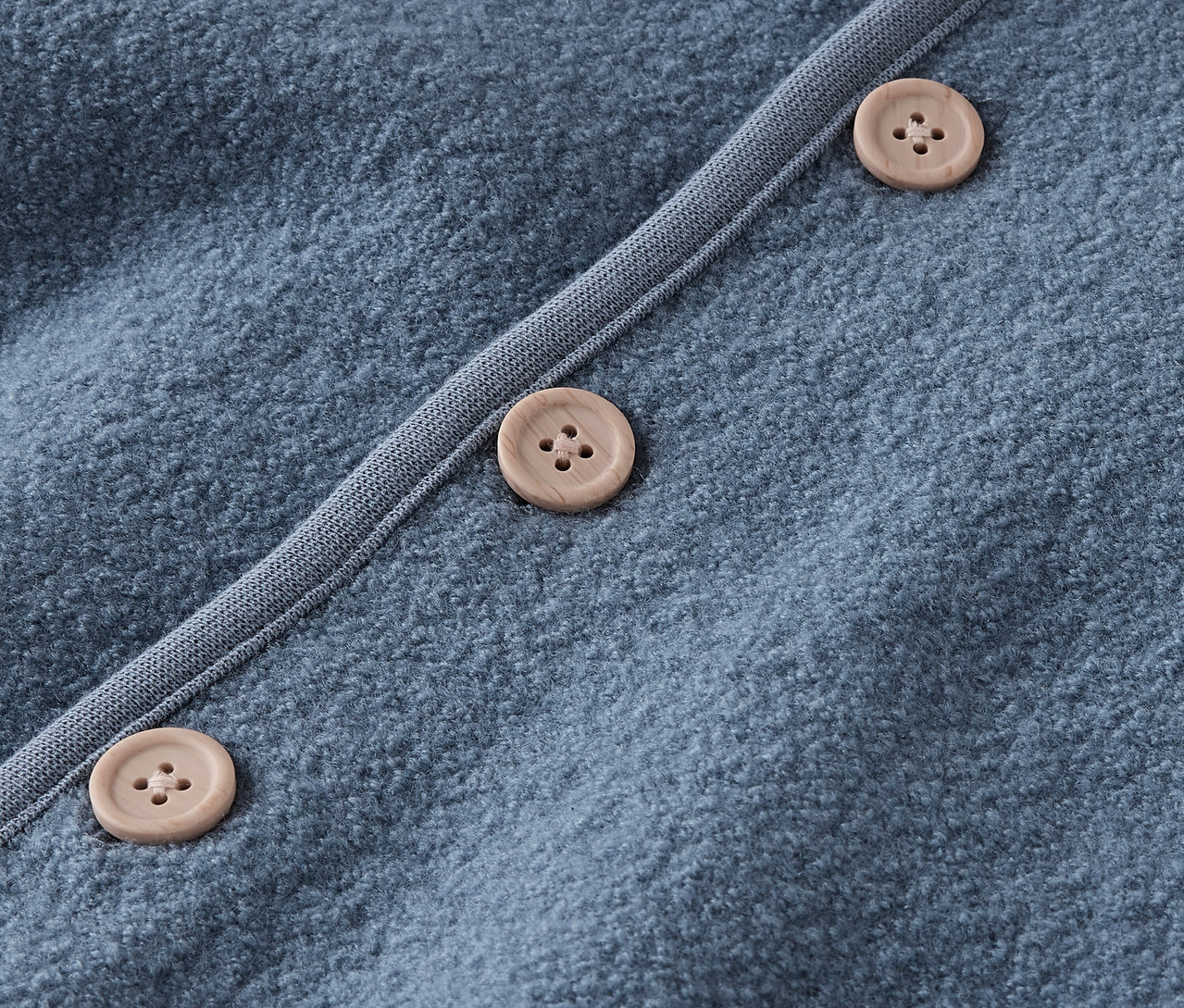 Gros plan d'un pull bleu avec des boutons marron.