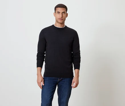 Un homme debout portant un pull noir et un jean bleu.
