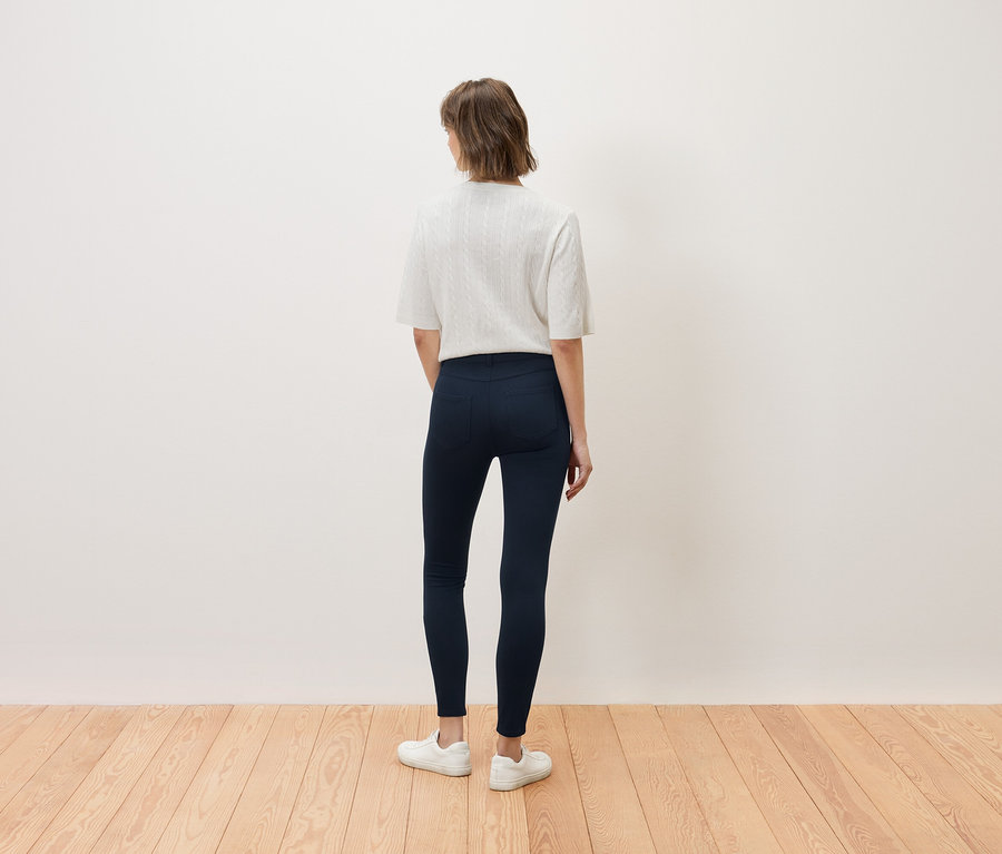 Une femme se tient dos à la caméra, portant un haut blanc et un jean bleu marine.