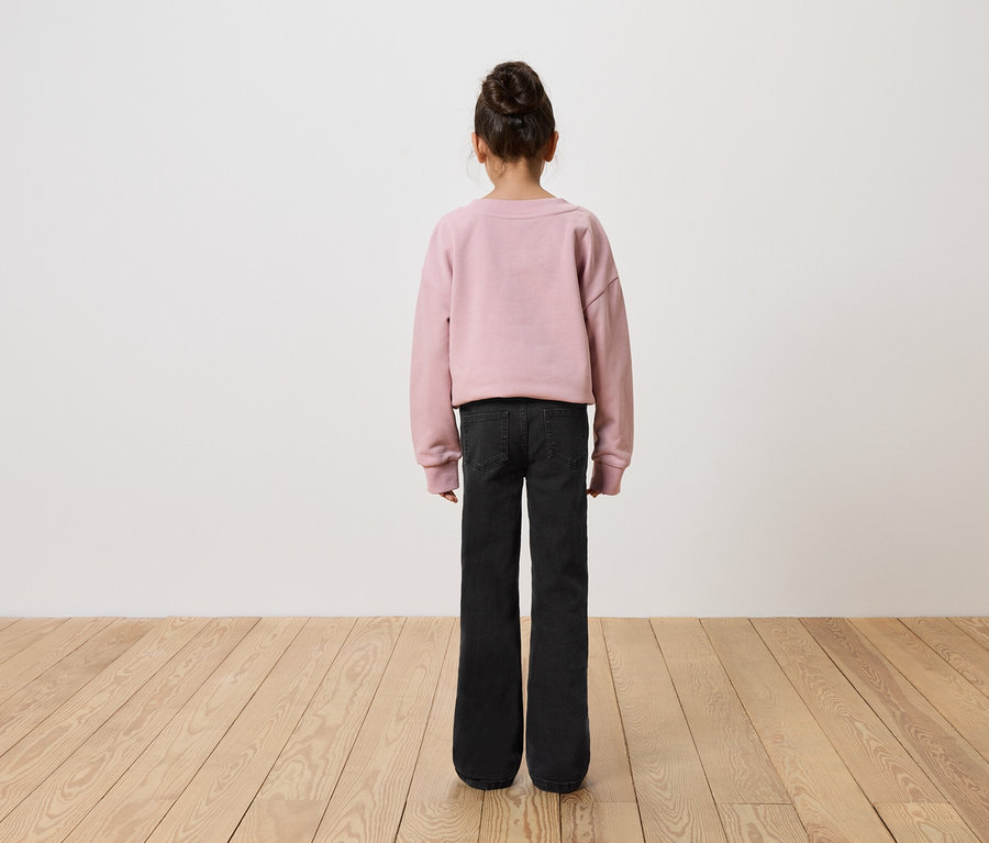 Une fille, vue de dos, porte un sweat-shirt rose et un jean noir.