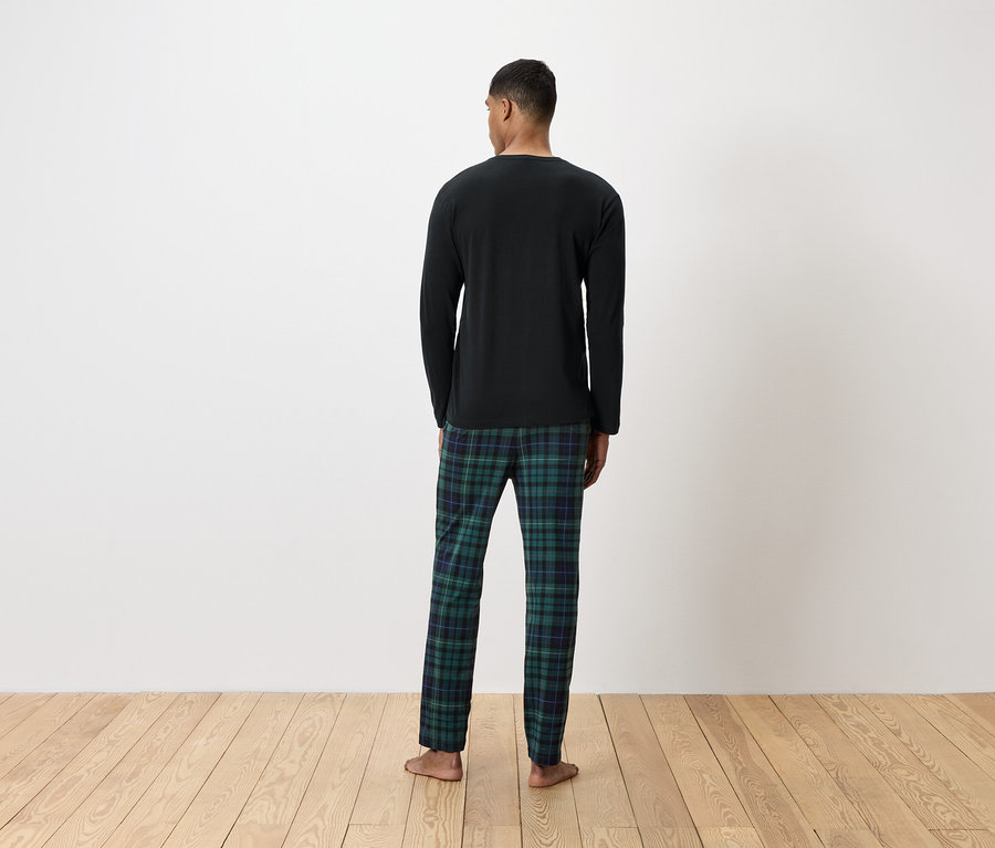 Un homme vu de dos porte un t-shirt noir à manches longues et un pantalon de pyjama à carreaux verts.