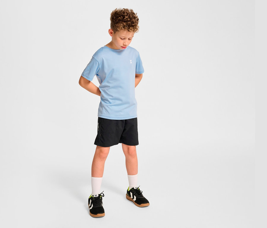 Garçon posant en t-shirt d’entraînement HUMMEL HMLJR pulse bleu clair et short noir.