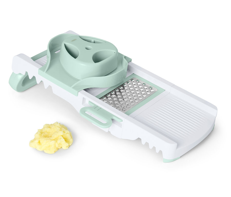 Une mandoline à découper blanche et verte avec un tas de légumes coupés.