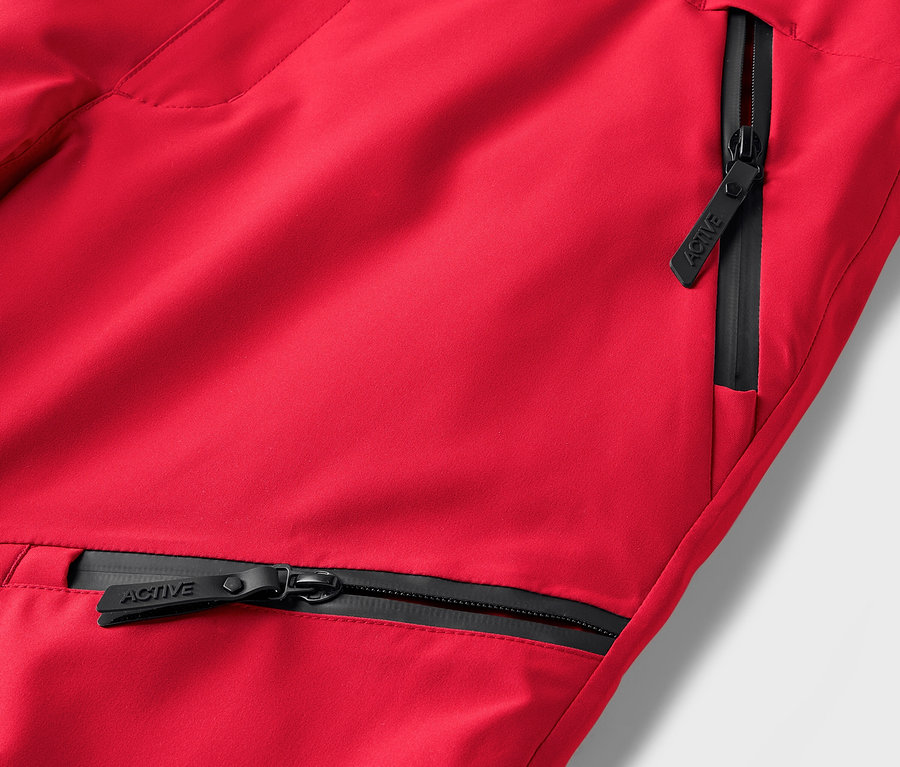 Détail d'un pantalon rouge avec des fermetures éclair noires sur les poches.