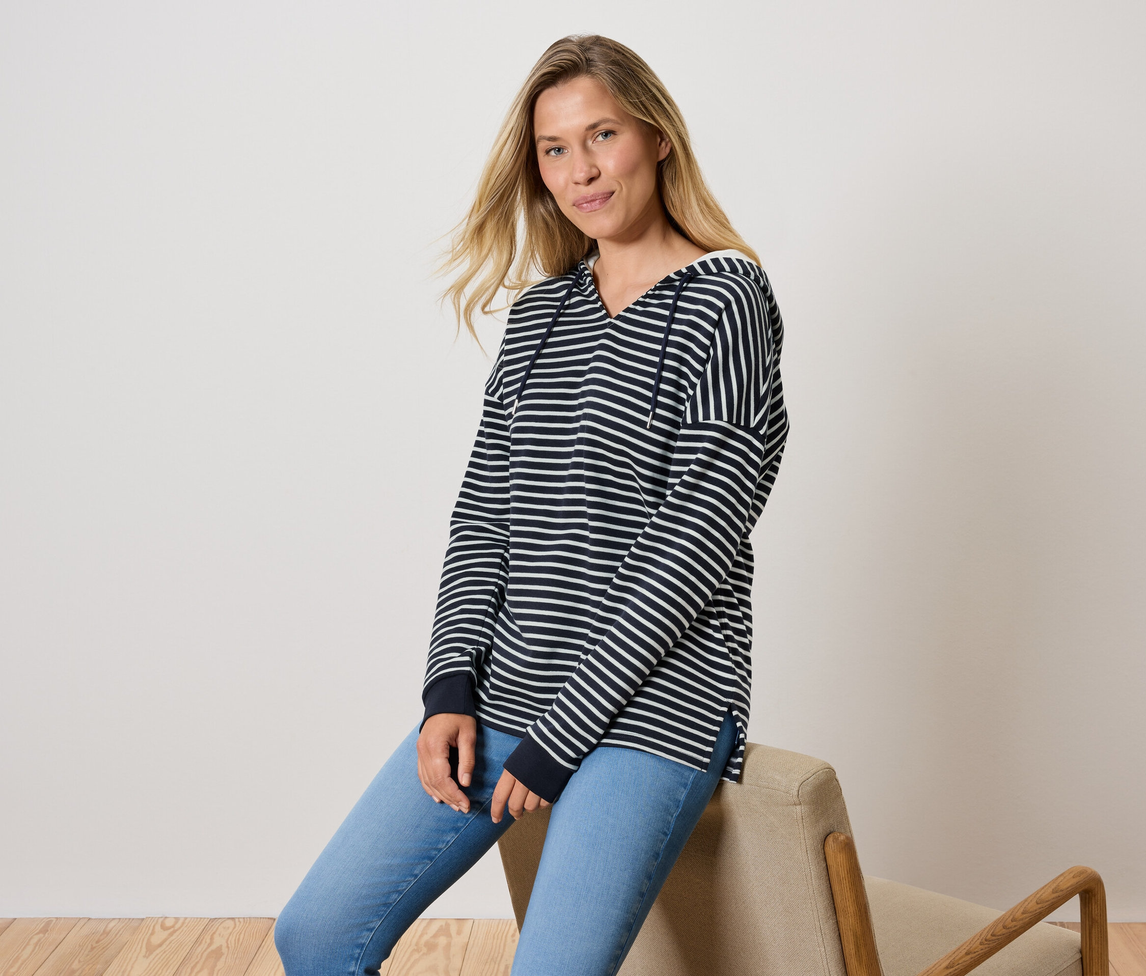 Une femme est assise sur une chaise, portant un jean bleu et un sweat à capuche rayé.