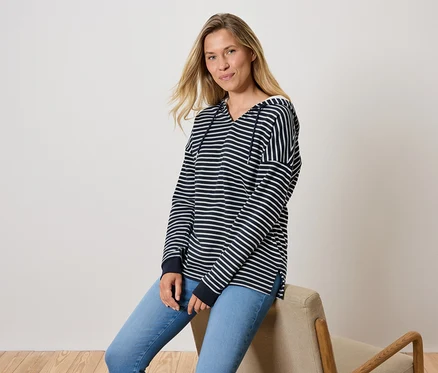 Une femme est assise sur une chaise, portant un jean bleu et un sweat à capuche rayé.