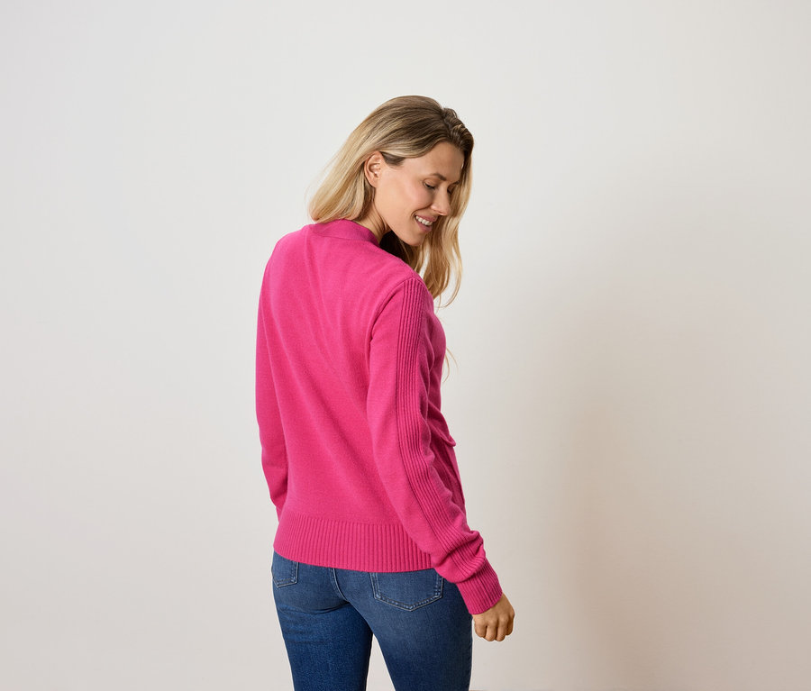 Une femme regarde vers le bas et porte un pull rose et un jean.