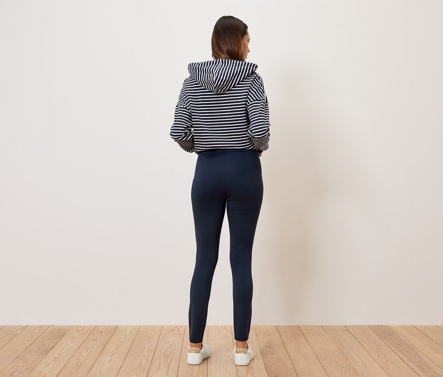 Une femme, vue de dos, porte un sweat à capuche rayé et un legging bleu marine.