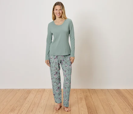Une femme debout portant un pyjama vert avec un motif floral.