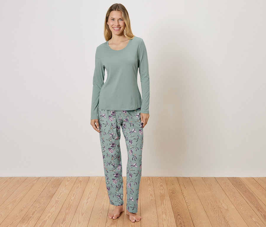 Une femme debout portant un pyjama vert avec un motif floral.