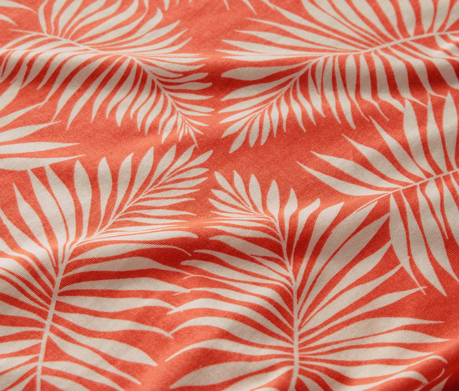 Gros plan d'une blouse imprimée avec un motif de feuilles de palmier blanches sur un fond corail.