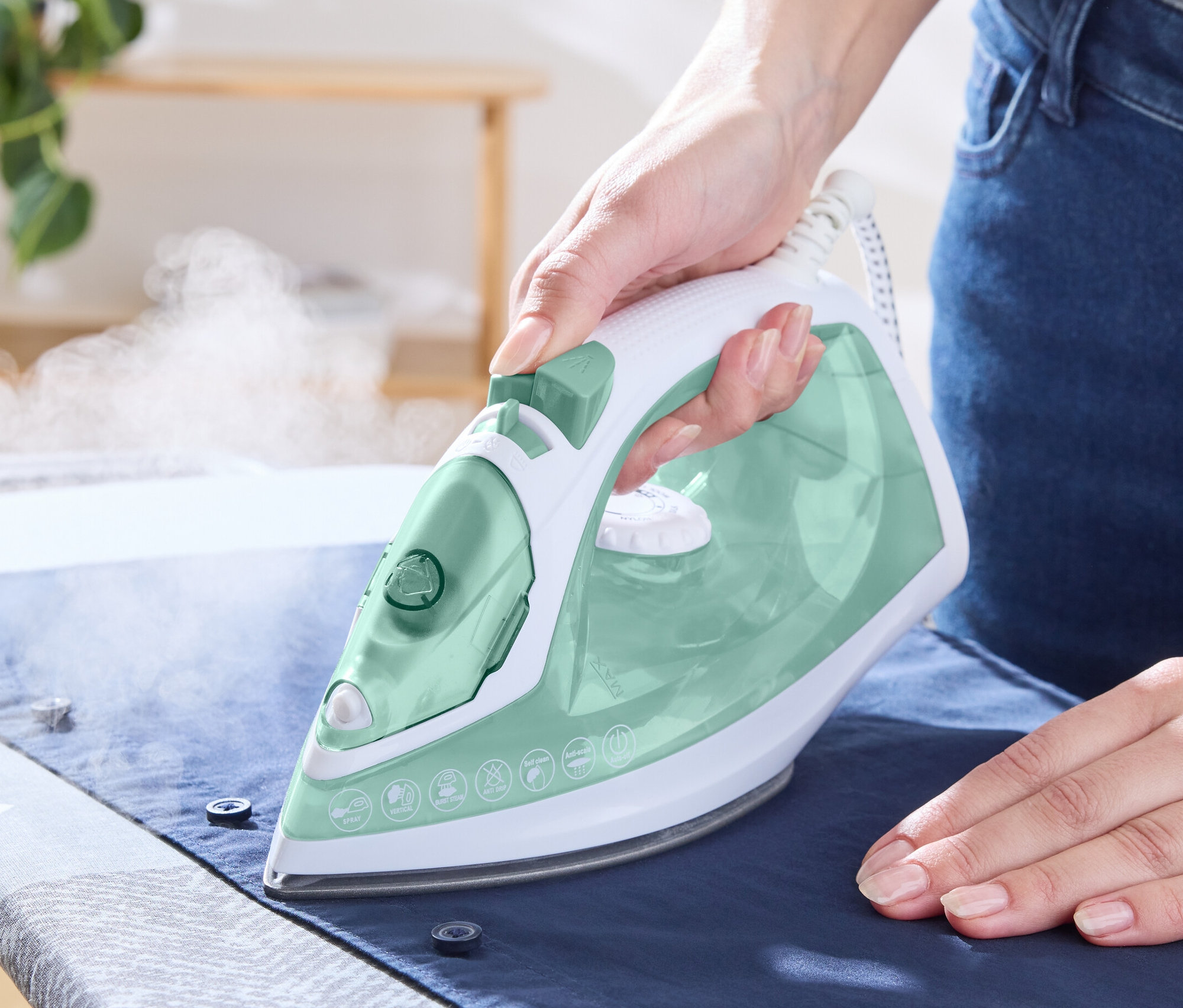 Une femme repasse une chemise avec un fer à repasser à vapeur.