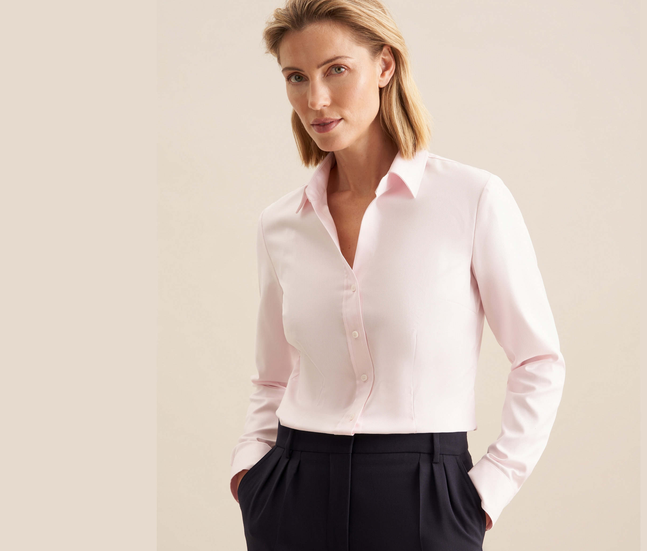 Une femme porte un chemisier en tulle rose Seidensticker et un pantalon bleu marine.