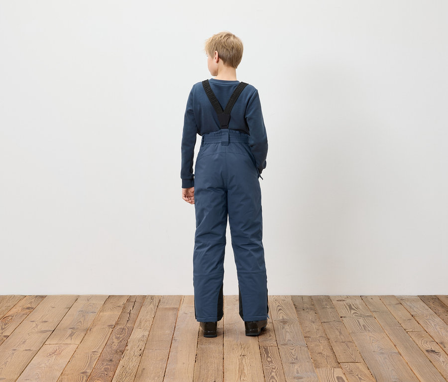 Un garçon, vu de dos, porte une salopette bleue.