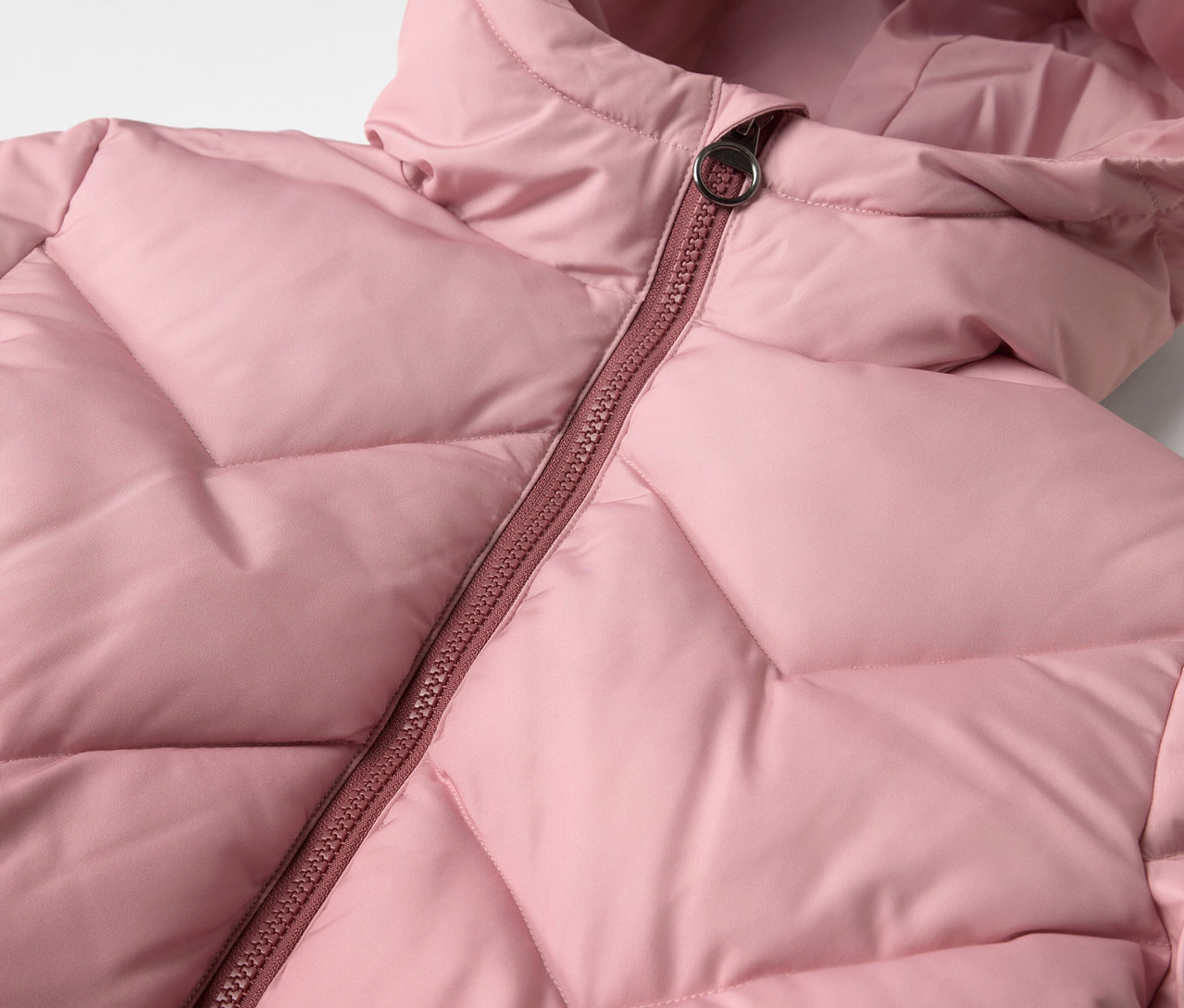 Gros plan sur un manteau thermique rose pour enfants avec capuche et fermeture éclair.
