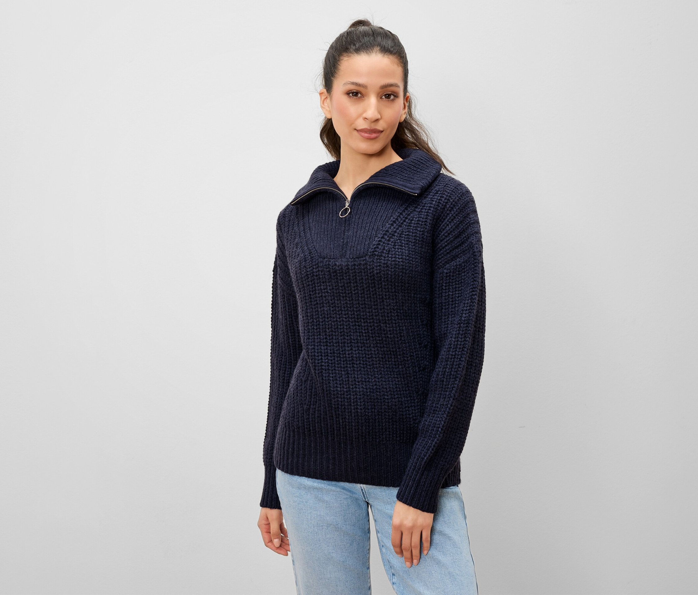Femme posant en pull en tricot bleu marine avec fermeture éclair et jean clair.