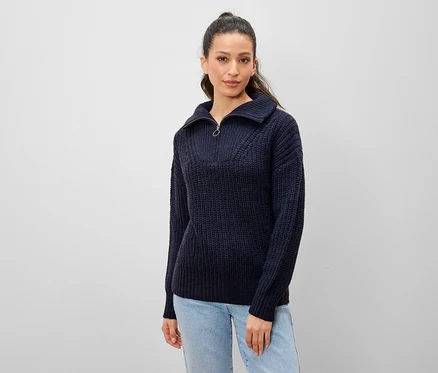 Femme posant en pull en tricot bleu marine avec fermeture éclair et jean clair.