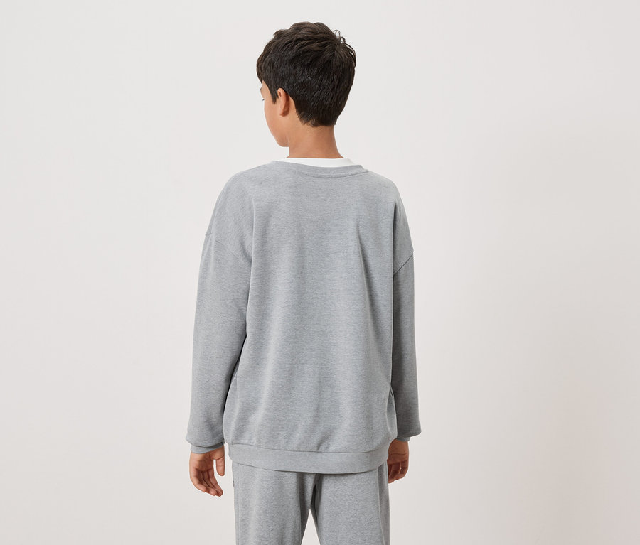 Un enfant aux cheveux foncés porte un sweat-shirt gris et un pantalon de survêtement gris, vu de dos.