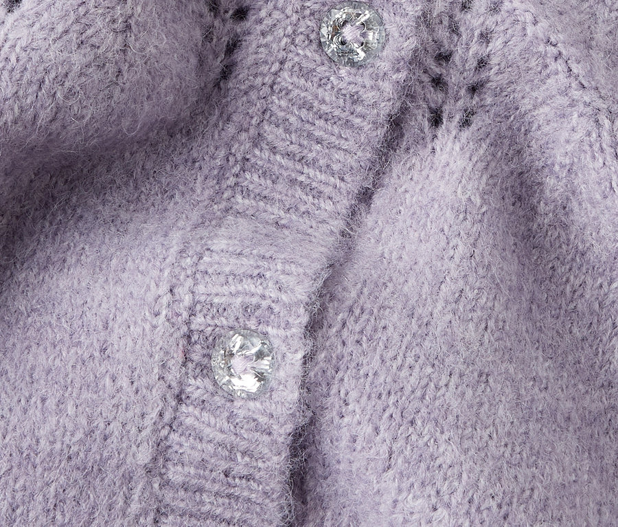 Gros plan sur un cardigan en tricot lilas avec deux boutons argentés.