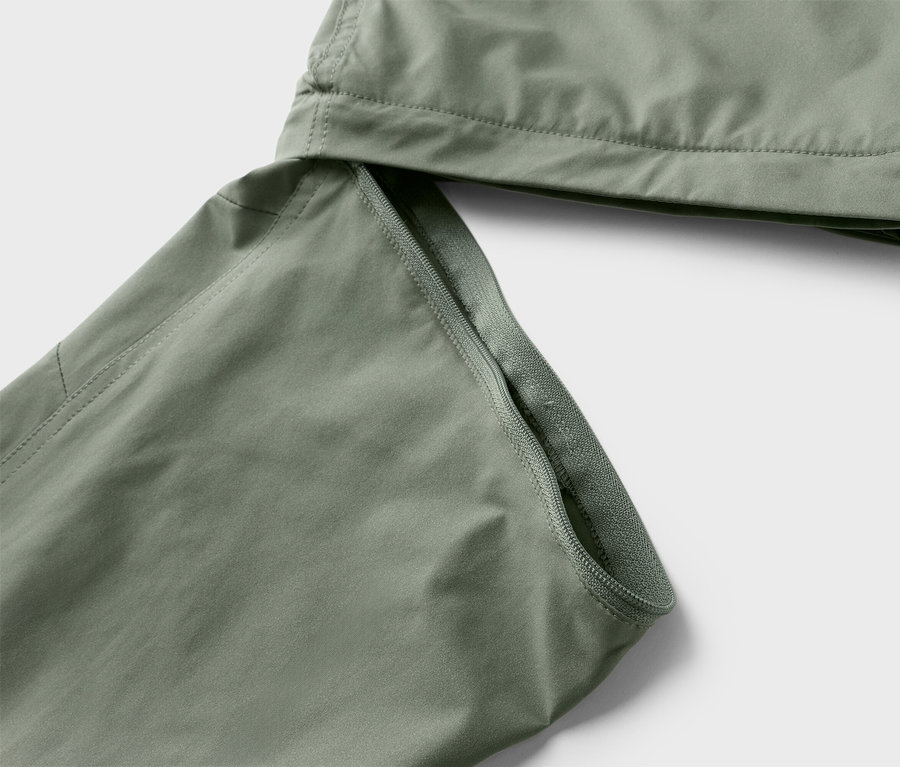 Gros plan sur des jambes de pantalon vert olive avec fermeture éclair sur fond neutre.