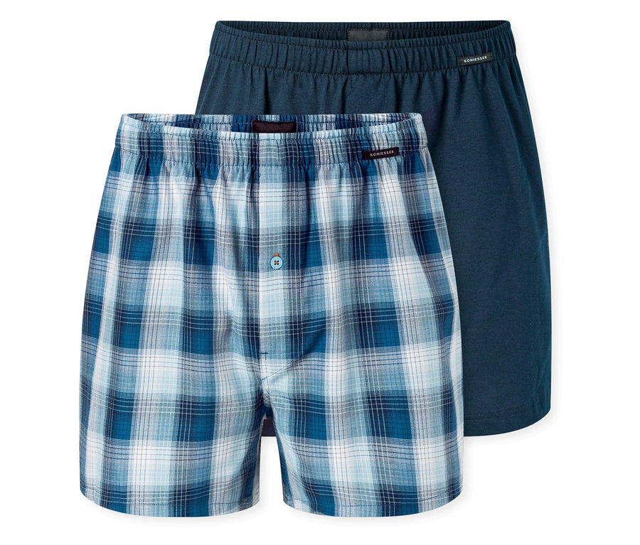Deux boxers tissés SCHIESSER. Celui de devant est à carreaux bleus et blancs avec un bouton, et celui de derrière est bleu foncé uni.