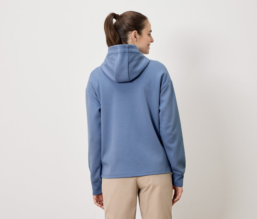 Une femme avec une queue de cheval porte un sweat à capuche bleu et un short beige.