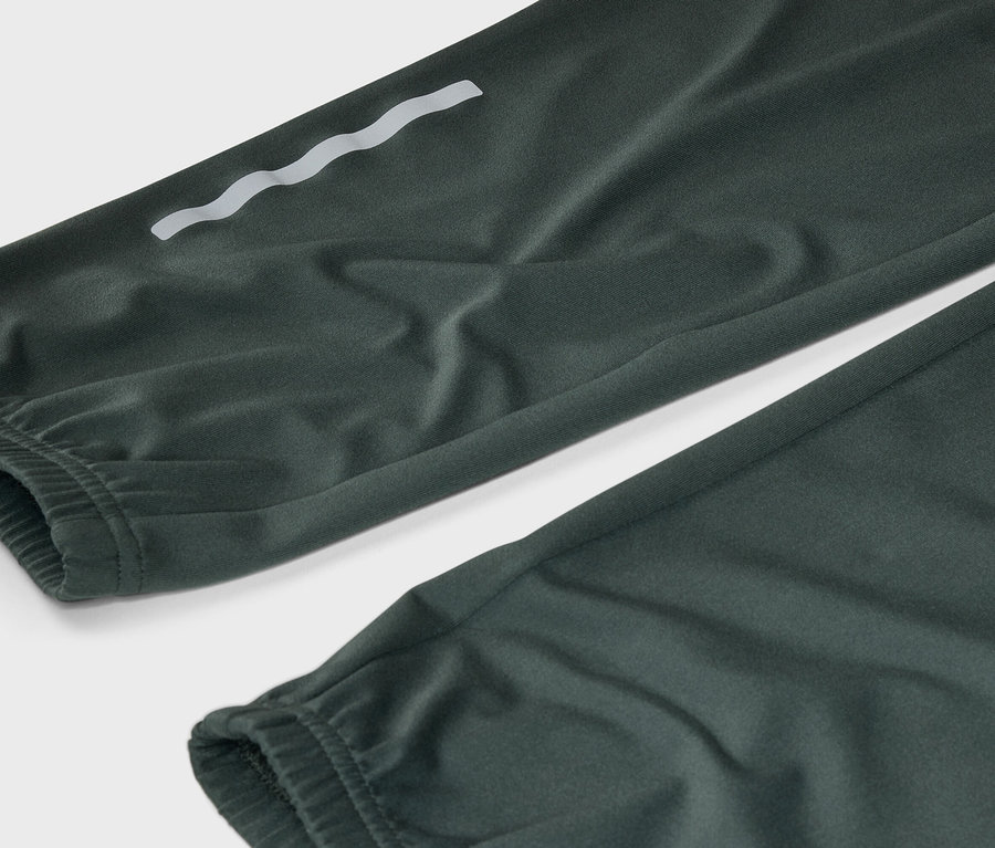 Gros plan sur un pantalon vert foncé avec des ourlets élastiques et un détail réfléchissant ondulé sur la jambe.