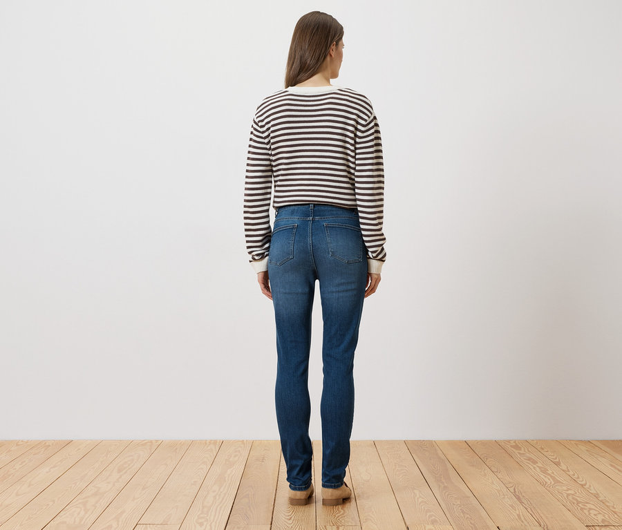 Une femme, vue de dos, porte un pull rayé, un jean et des chaussures.