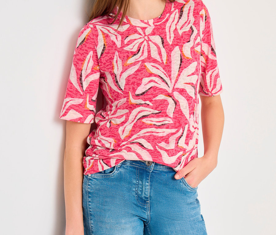 Femme portant un t-shirt manches courtes CECIL rose à motif abstrait blanc et noir, un jean bleu et tenant un sac gris foncé.